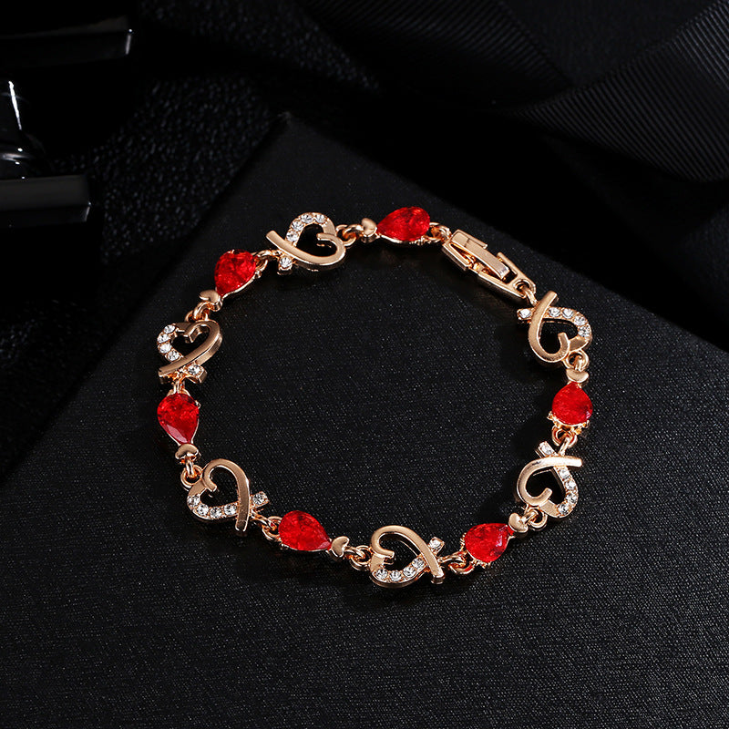 Rose gold heart rhinestone bracelet with red teardrop stones and linked heart charms.