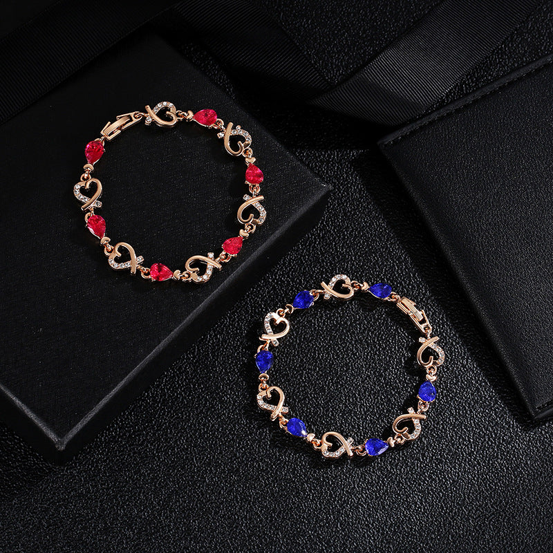 Rose gold heart rhinestone bracelet with red and blue teardrop stones on linked charms.