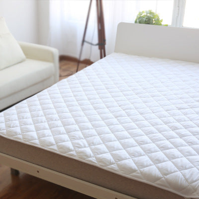 White quilted mattress topper with diamond stitching, placed on a bed