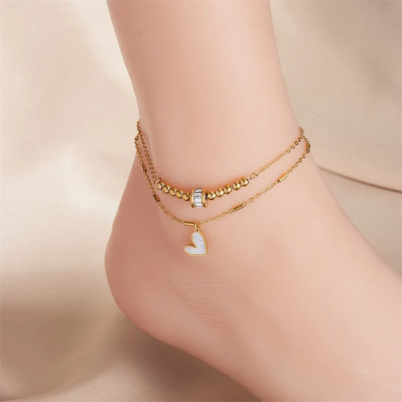 Gold heart anklet worn on ankle, featuring two linked chains and hanging heart charm
