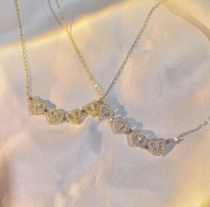 Gold clover-heart necklace with linked heart crystals along the chain
