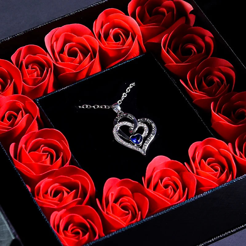 Blue crystal heart necklace pendant with chain on black insert surrounded by red roses