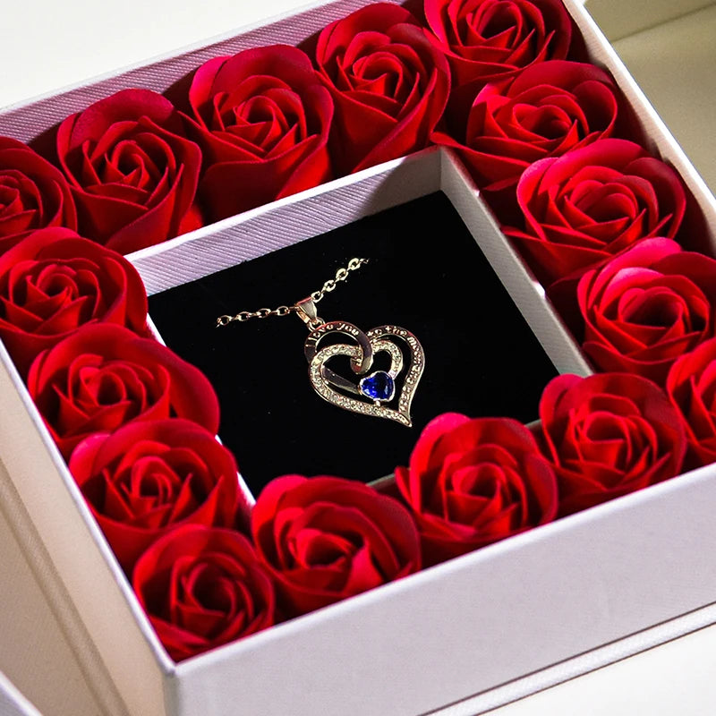 Heart necklace pendant with blue crystal resting on red rose-filled jewelry box insert